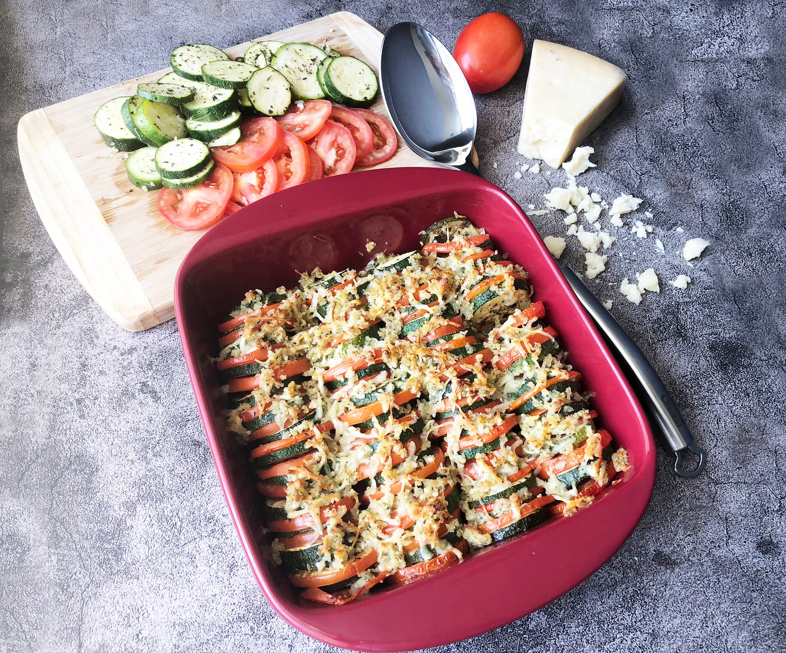 cooked zucchini and tomato bake in red ceramic square oven dish